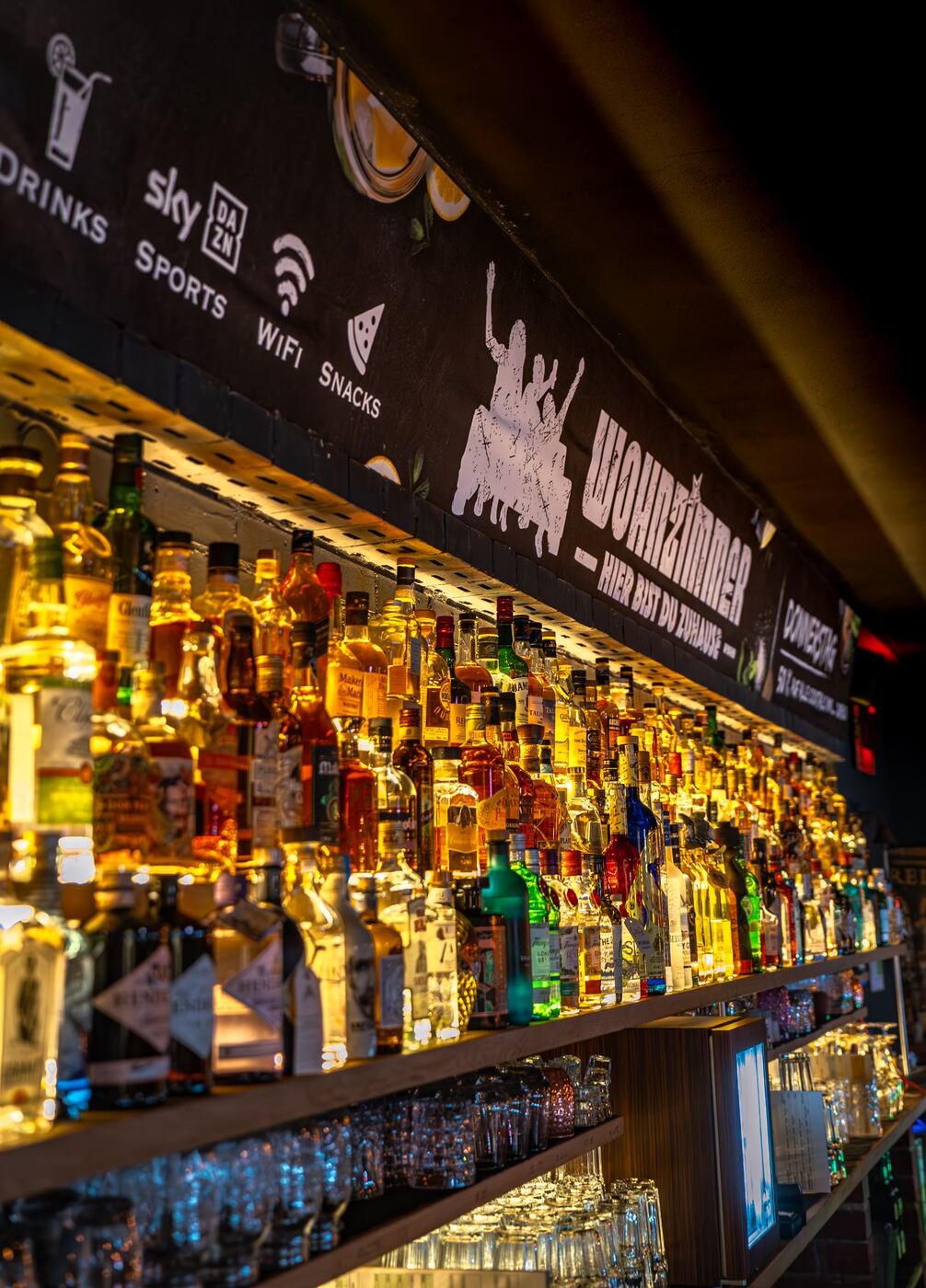 Cocktailbar Coburg: beleuchtete Backbar der Wohnzimmer Bar mit Whiskey, Gin und Rum